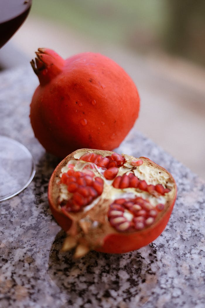 gallery-03 Vibrant red pomegranates displayed on a granite surface, showcasing their rich seeds.